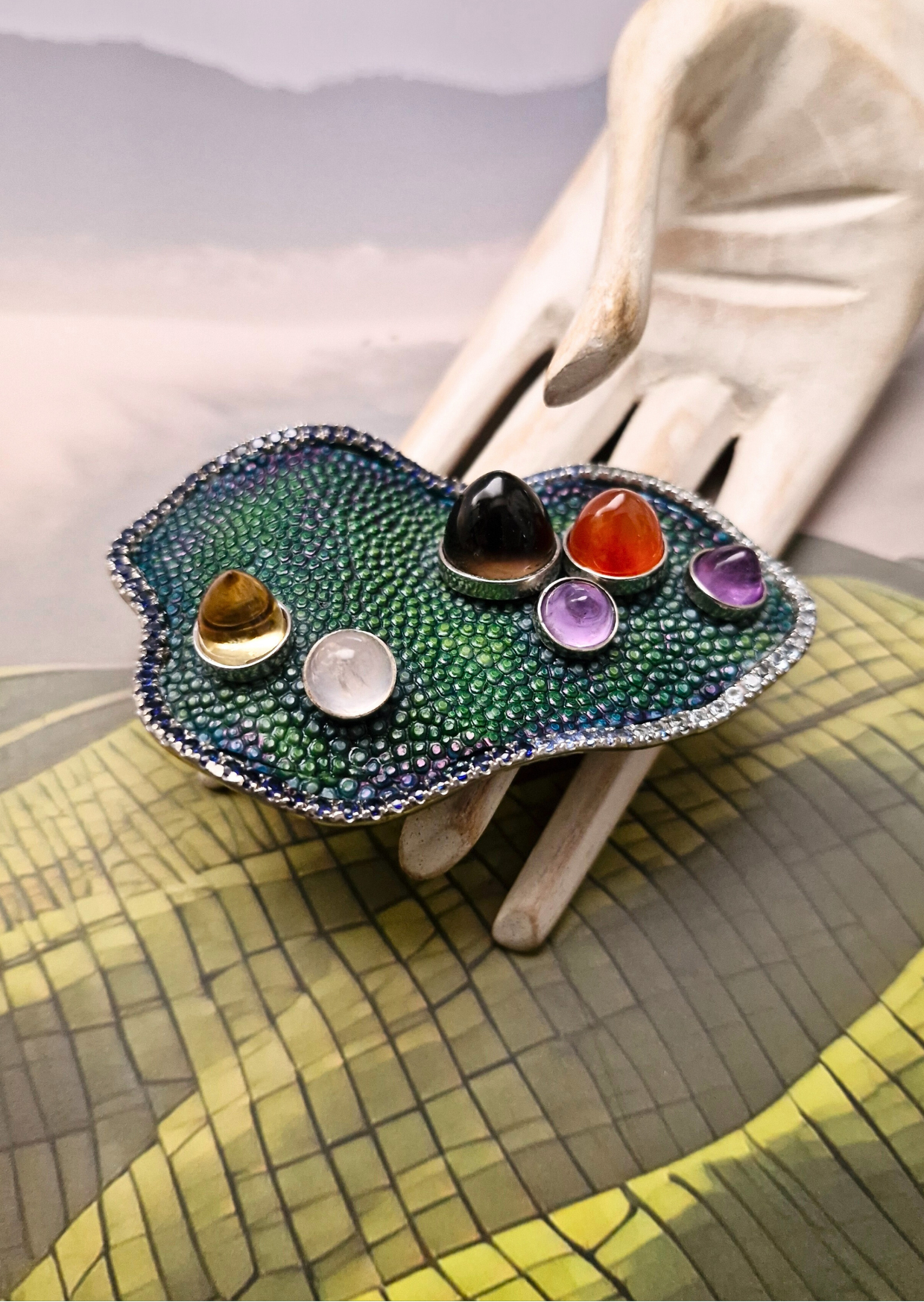 Colorful gemstone ring on a white surface with a yellow and green patterned fabric background
