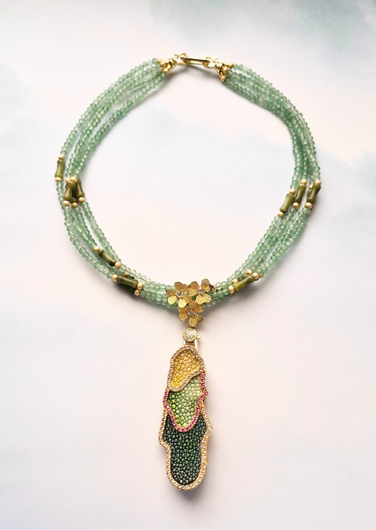 Green beaded necklace with gemstone and stingray leather accents on a white background